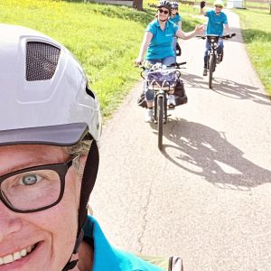 Drei Menschen fahren mit dem Fahrrad auf einem sonnigen Feldweg.
