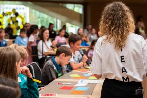 Eine junge Frau leitet eine Gruppe Kinder an, die im Landtag etwas erarbeitet.